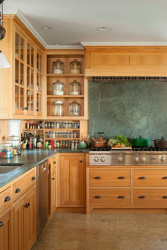 a stained kitchen with flat panel and shaker cabinets, grey soapstone countertops and a blacksplash, stainless steel countertops