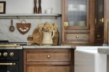 a stained kitchen with shaker and fluted glass cabinets, a white stone backsplash and countertops, elegant brass fixtures is amazing