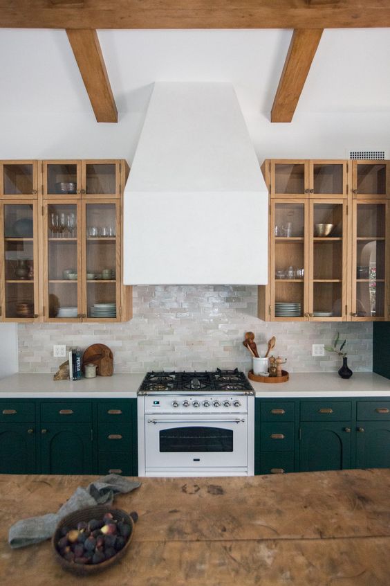 a stylish kitchen with dark green and stained kitchen cabinets, arches and glass ones, with a glossy tile backsplash and a white hood