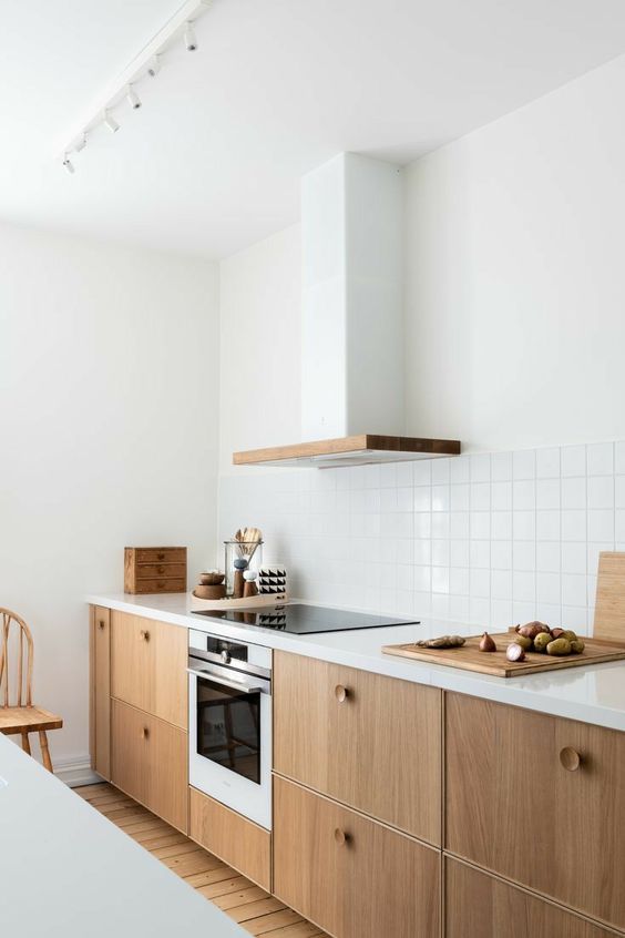 a stylish light-stained flat panel kitchen with wooden knobs, white stone countertops, a white square tile backsplash