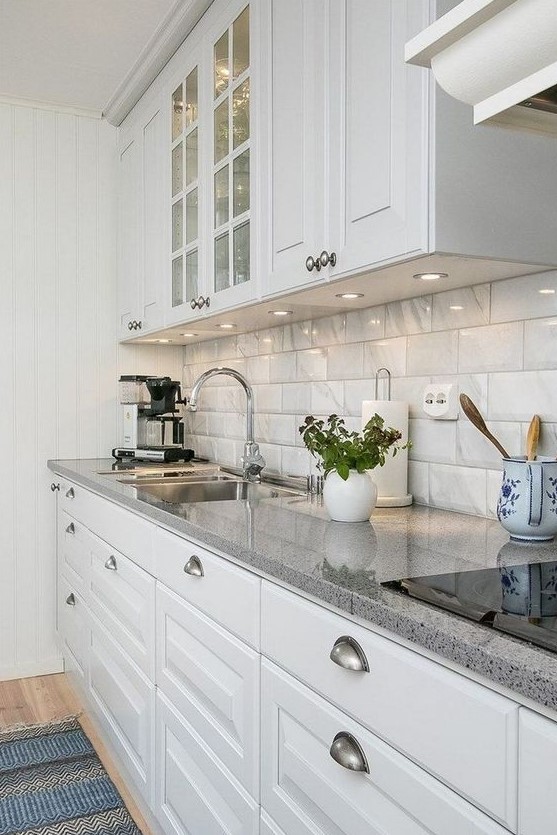 a stylish modern kitchen in white, with glossy tiles on the backsplash and grey granite countertops plus built-in lights is chic