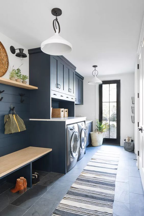 a stylish navy laundry mudroom with shaker cabinets, a washing machine and a dryer, a built-in bench and an open shelf