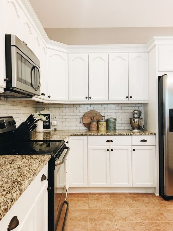 a stylish white kitchen with granite countertops, a white tile backsplash and black knobs and fixtures