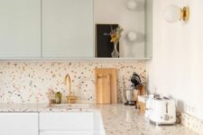 a sutble kitchen with white and light green flat panel cabinets, a colorful terrazzo countertop and a backsplash, touches of gold