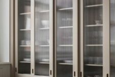 a tan kitchen with shaker cabinets and fluted glass upper cabinets for storing dishes is a chic and stylish space