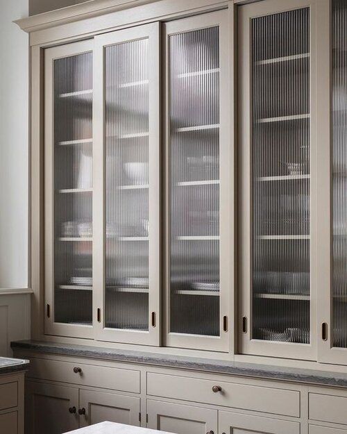 a tan kitchen with shaker cabinets and fluted glass upper cabinets for storing dishes is a chic and stylish space