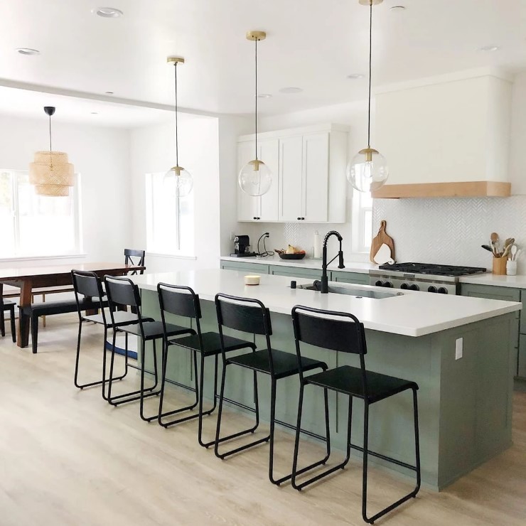 a trendy two-tone kitchen with shaker cabinets, a large white hood, a large kitchen island and black fixtures and stools