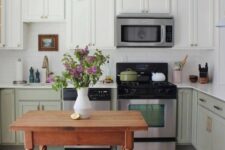 a two-tone kitchen with white and sage green cabinets, a white tile backsplash and countertops and a small table as a kitchen island