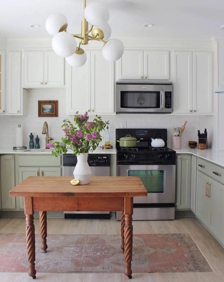 a two-tone kitchen with white and sage green cabinets, a white tile backsplash and countertops and a small table as a kitchen island