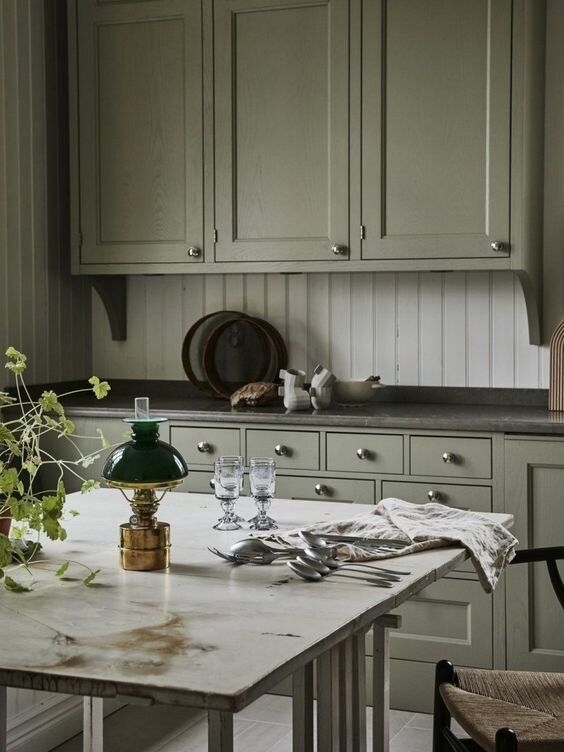 a vintage green kitchen with grey soapstone countertops, a white stone table, a white beadboard backsplash is amazing