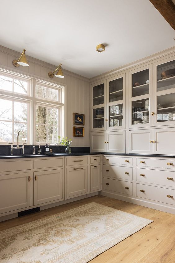 a vintage-inspired tan kitchen with shaker cabinets, black soapstone countertops, vintage fixtures and sconces