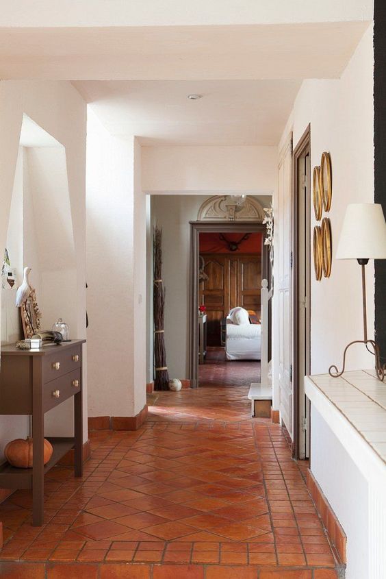 a vintage space with a terracotta tile floor, a dark-stained console table, decorative plates and a vintage lamp