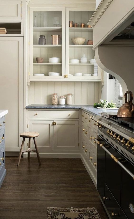 a vintage tan-colored kitchen with inlay and glass cabinets, dark stone countertops and a beadboard backsplash plus a vintage black cooker