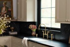 a vintage tan kitchen with black soapstone countertops and a backsplash, a vintage artwork and some lovely decor