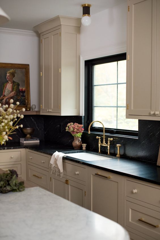 a vintage tan kitchen with black soapstone countertops and a backsplash, a vintage artwork and some lovely decor