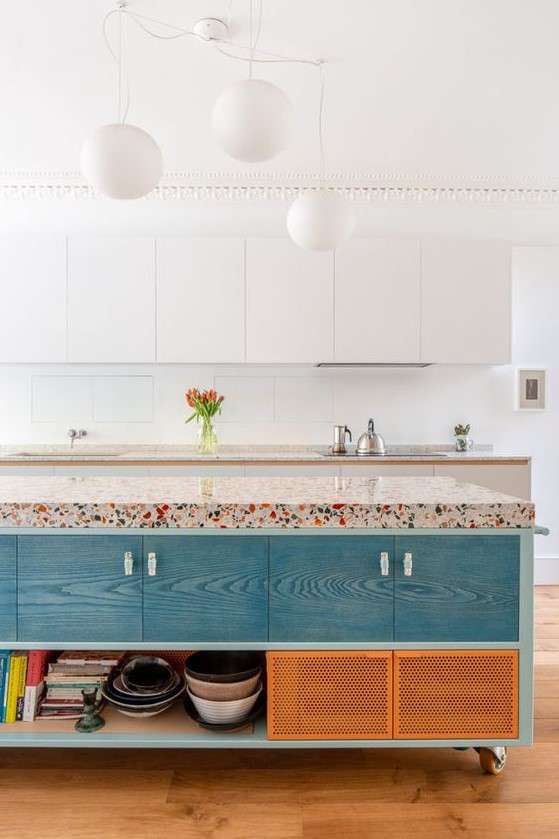 a vivacious kitchen with white sleek cabinets, a colorful kitchen island with a bright terrazzo countertop and pendant lamps