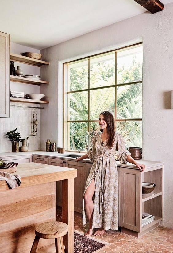 a welcoming kitchen with a large window, a terracotta tile floor, light-stained cabinets, open shelves and a large kitchen island