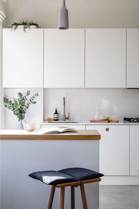 a white Scandinavian kitchen with a sleek white backsplash, a kitchen island with a butcherblock countertop