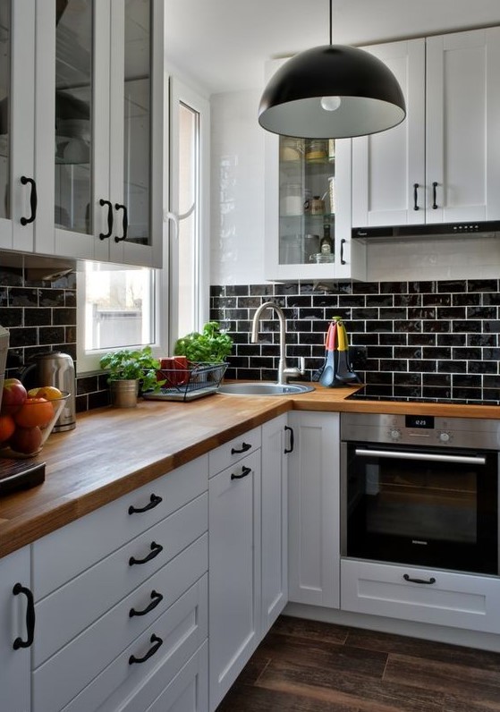 a white farmhouse kitchen with a black glazed tiles, butcherblock countertops, black pendant lamps