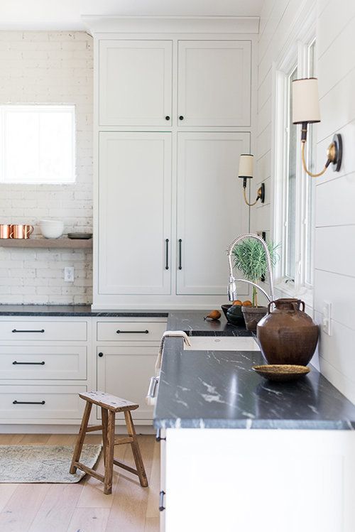 a white farmhouse kitchen with shaker cabinetry, black soapstone countertops, a white brick backsplash and open shelves