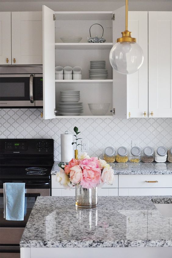 a white farmhouse kitchen with shaker cabinets, a white arabesque tile backsplash, white granite countertops and chic pendant lamps