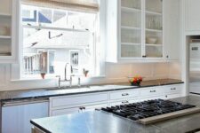 a white farmhouse kitchen with shaker cabinets, black soapstone countertops, a window as a backsplash