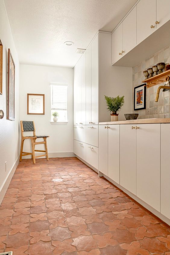 a white galley kitchen with sleek cabinets made more eye-catchy with a terracotta tile floor, butcherblock countertops and artwork