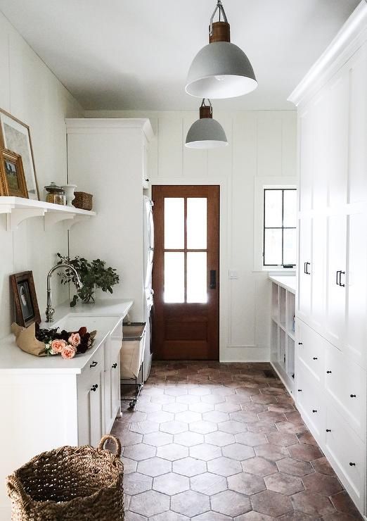 a white laundry room with a terracotta tile floor, white storage cabinets, baskets and shelves, pendant lamps