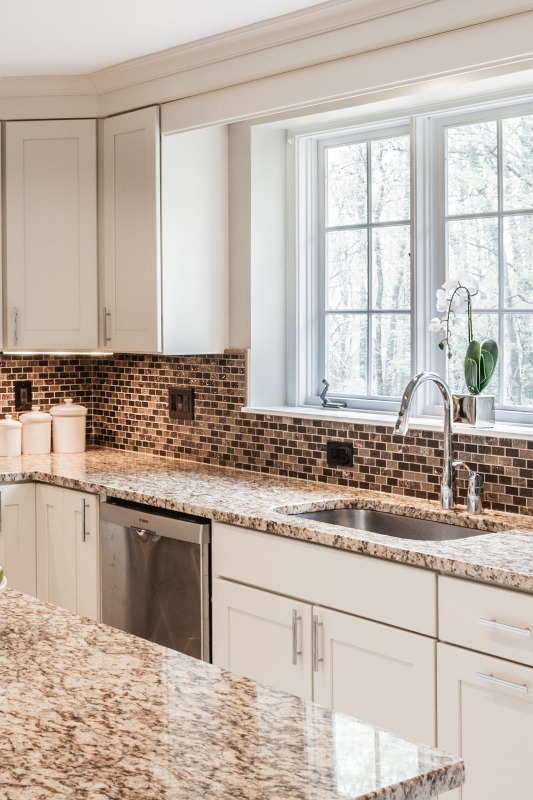 a white modern farmhouse kitchen with a tan small tile backsplash, beige and white granite countertops