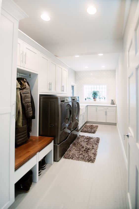 a white mudroom laundry with shaker cabinets, a washing machine and a dryer, a bench with open storage and fluffy rugs