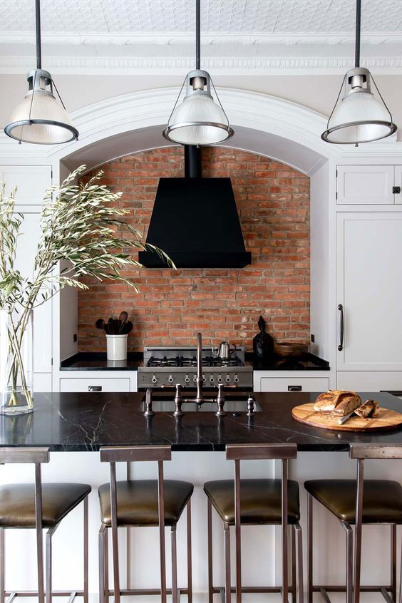 a white shaker style kitchen with a matching kitchen island, black soapstone countertops, elegant pendant lamps and dark stools