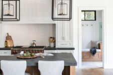 a white shaker style kitchen with a stained kitchen island, black soapstone countertops, framed hanging lamps over the island