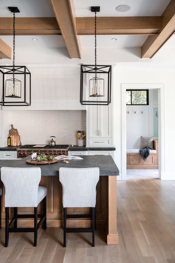 a white shaker style kitchen with a stained kitchen island, black soapstone countertops, framed hanging lamps over the island