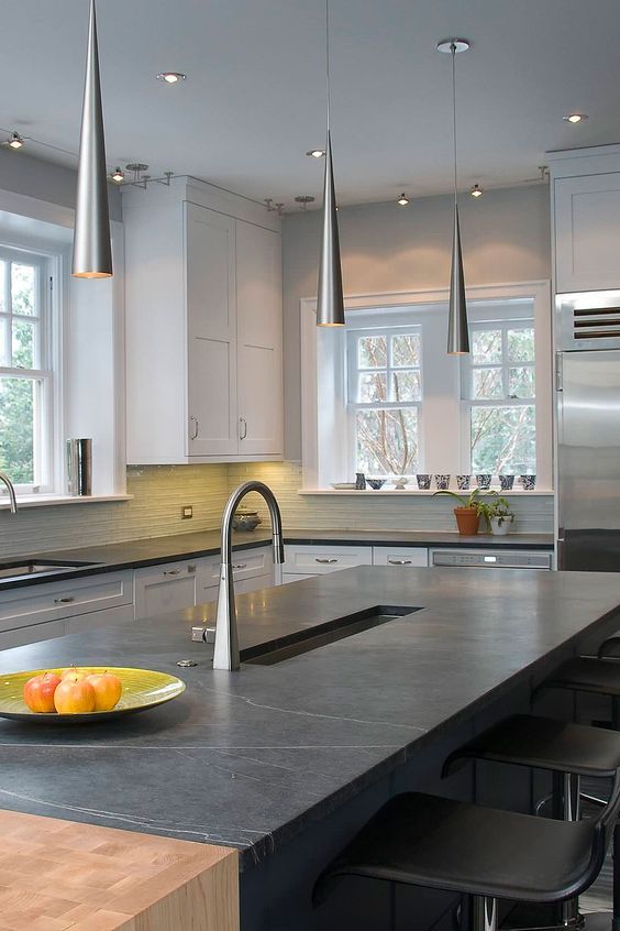 a white shaker style kitchen with a tile backsplash and black soapstone countertops and catchy pendant lamps over the island