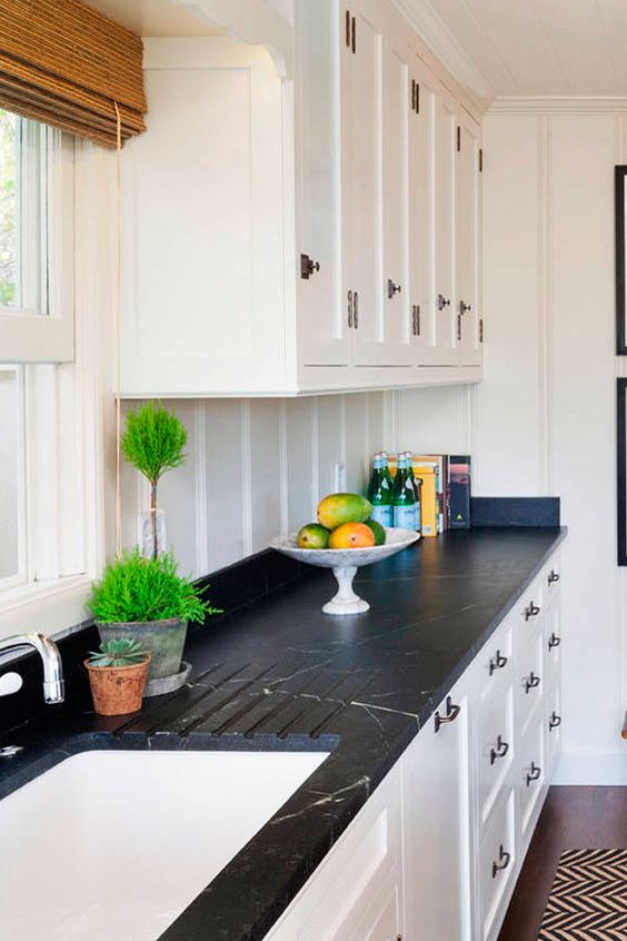 a white shaker style kitchen with a white beadboard backsplash, black soapstone countertops and black fixtures