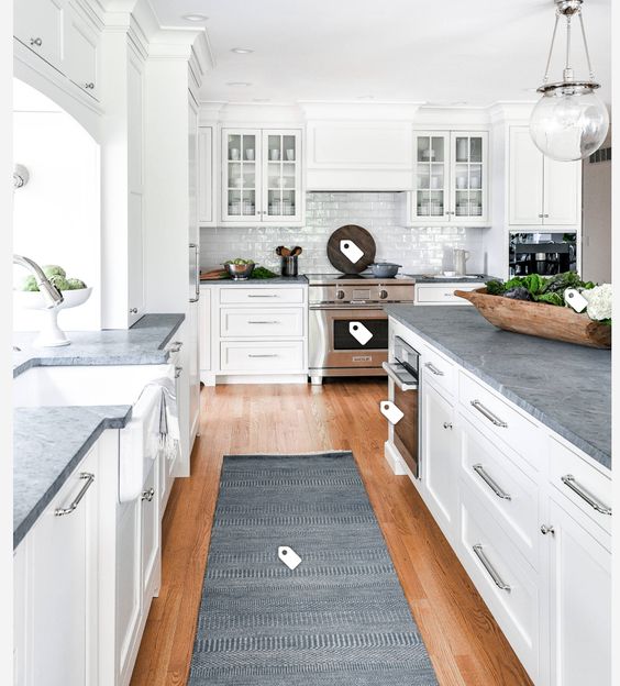 a white shaker style kitchen with a white glossy tile backsplash, grey soapstone countertops and pendant lamps