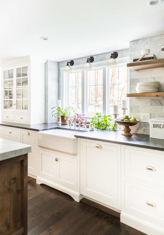 a white shaker style kitchen with black soapstone countertops, a white marble tile backsplash and open shelves