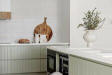 an airy contemporary kitchen with lower sage green slatted cabinets, a white skinny tile backsplash and white stone countertops