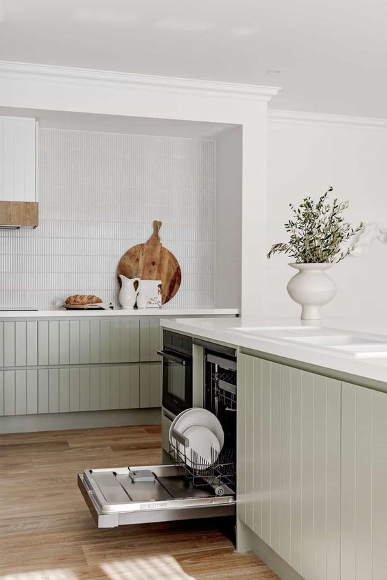 an airy contemporary kitchen with lower sage green slatted cabinets, a white skinny tile backsplash and white stone countertops