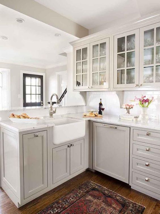 an airy grey kitchen with inlay and glass cabinets, a white subway tile backsplash and white quartz countertops