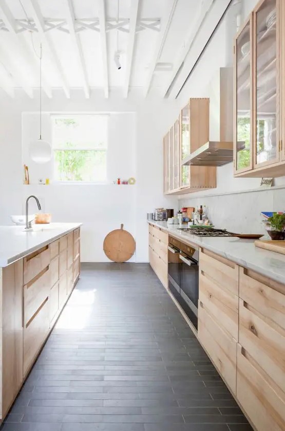 an airy light wood kitchen with sleek and glass cabinets, white stone countertops and a backsplash, stainless steel applainces