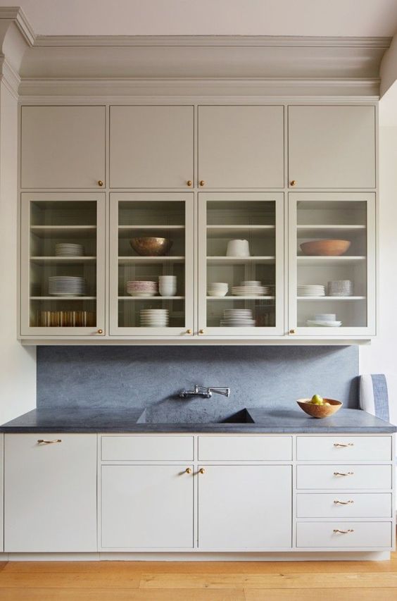 an airy neutral kitchen with flat panel and glass cabinets, black stone countertops and a backsplash, brass handles