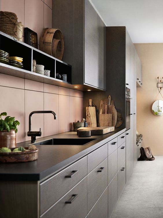 an elegant dark-stained kitchen with black soapstone countertops and a matte pink tile backsplash plus black fixutres