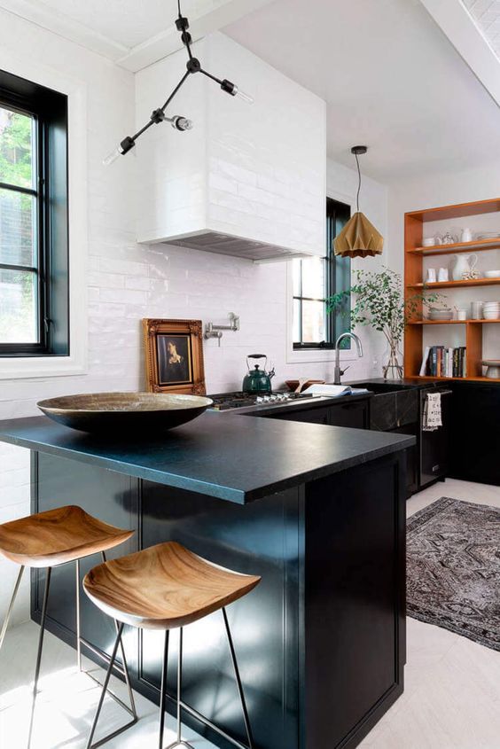 an elegant kitchen with flat panel lower cabinets, a white tile backsplash and a hood, black soapstone countertops and a stained shelf