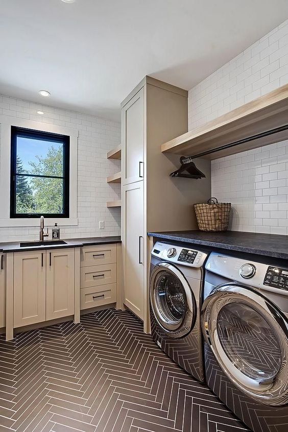 an elegant modern farmhouse mudroom laundry with tan shaker cabinets, black countertops, open shelves and a washing machine and a dryer