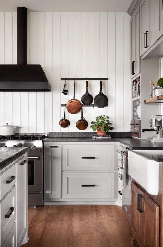 an elegant vintage dove grey kitchen with shaker cabinets, open shelves, a black hood and black soapstone countertops