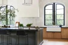an elegant vintage kitchen with stained cabinets, a black kitchen island, a white hood and arched window with black frames
