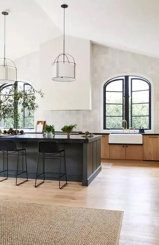 an elegant vintage kitchen with stained cabinets, a black kitchen island, a white hood and arched window with black frames