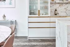an exquisite white kitchen with flat panel and fluted glass cabinets, a white kitchen island, white stone countertops and a backsplash