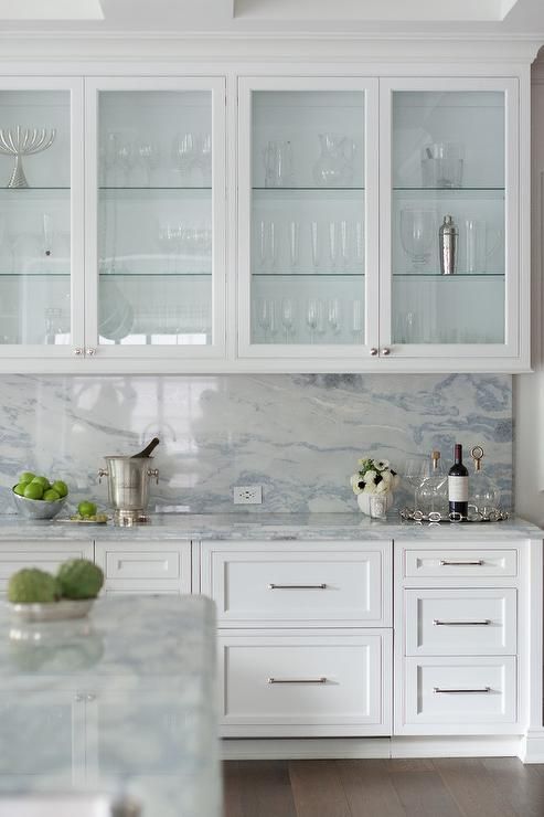 an exquisite white kitchen with inlay and glass cabinets, a white and blue quartz backsplash and countertops is wow